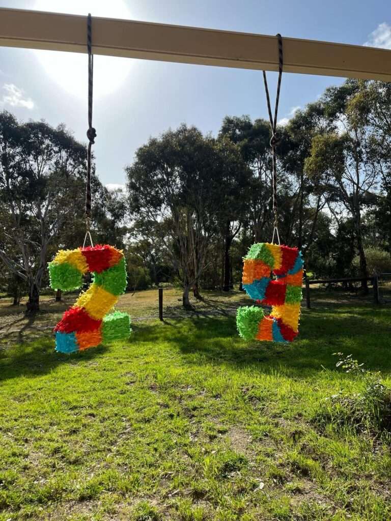 Two piñatas in the shape of a 2 and a 9 hanging from a metal beam.