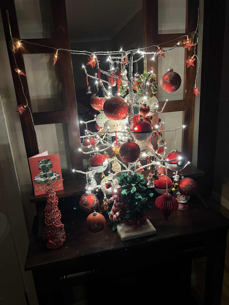A red and white Christmas tree on a wooden vanity, complete with lights and ornaments.
